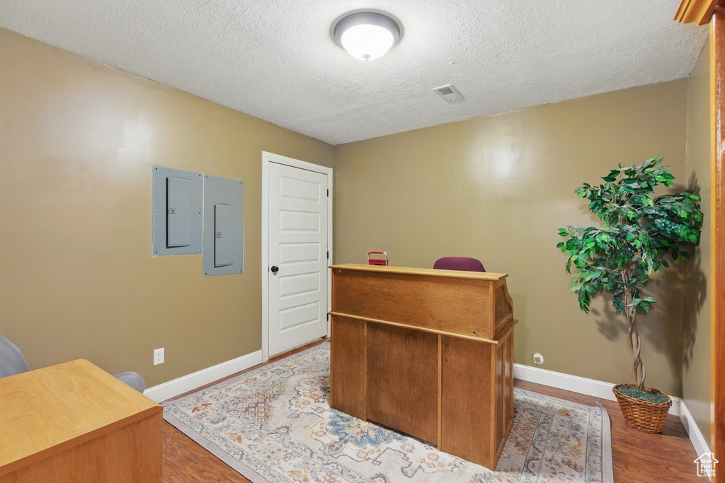 Office with baseboards, a textured ceiling, wood finished floors, and electric panel