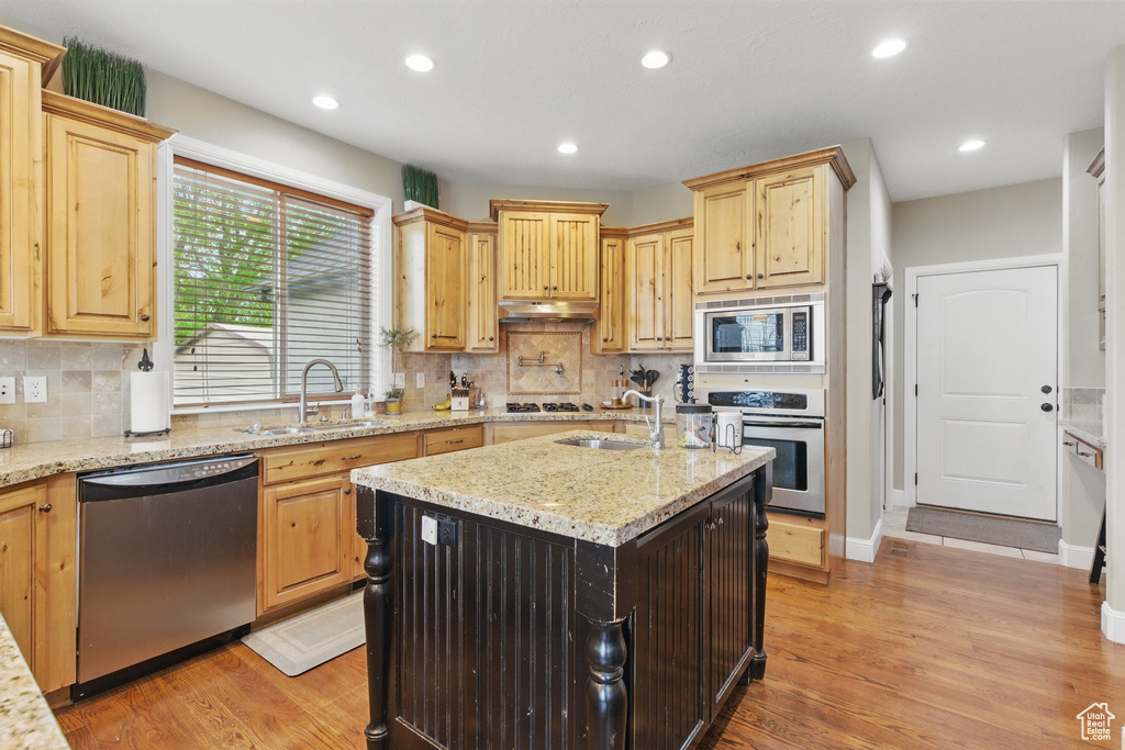 Kitchen featuring under cabinet range hood, stainless steel appliances, light brown cabinetry, and a sink