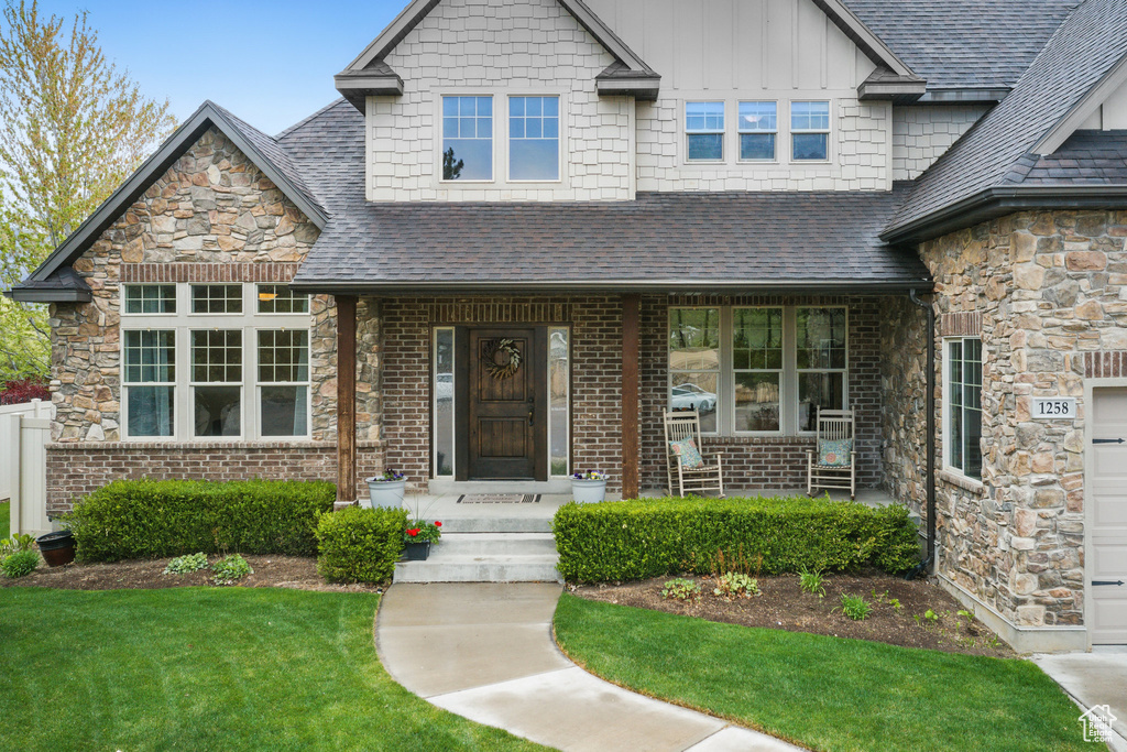 View of front of house featuring board and batten siding, roof with shingles, stone siding, and a front yard