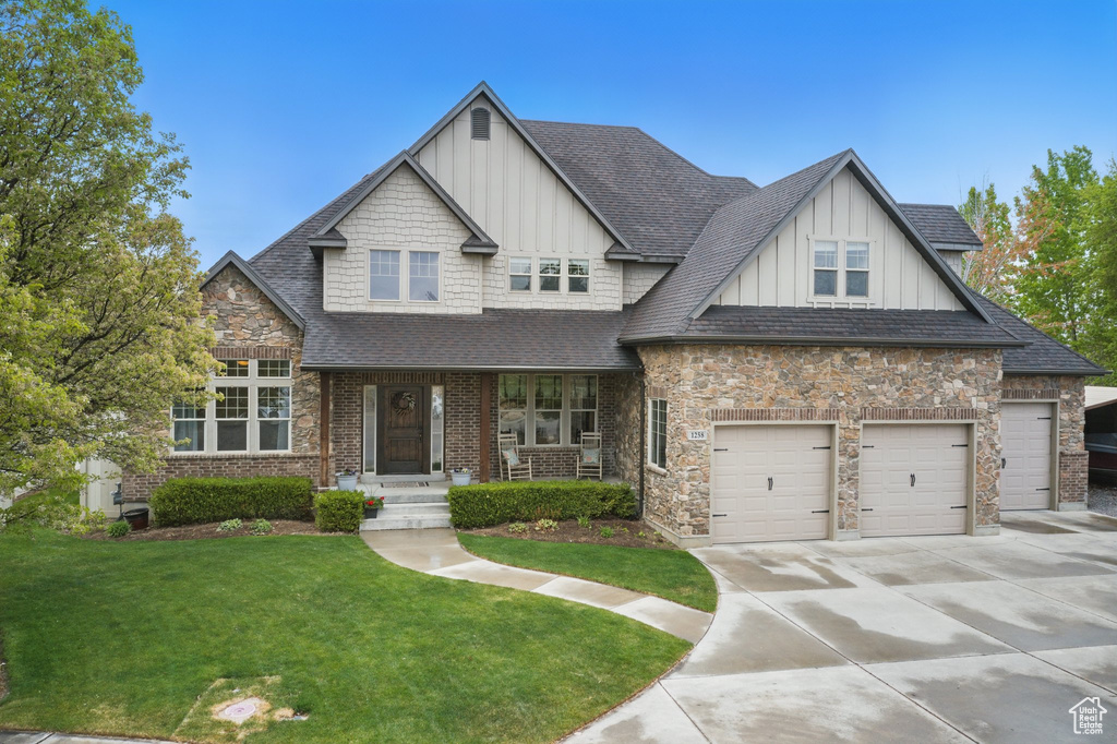 Craftsman-style house with board and batten siding, roof with shingles, a garage, a front lawn, and concrete driveway