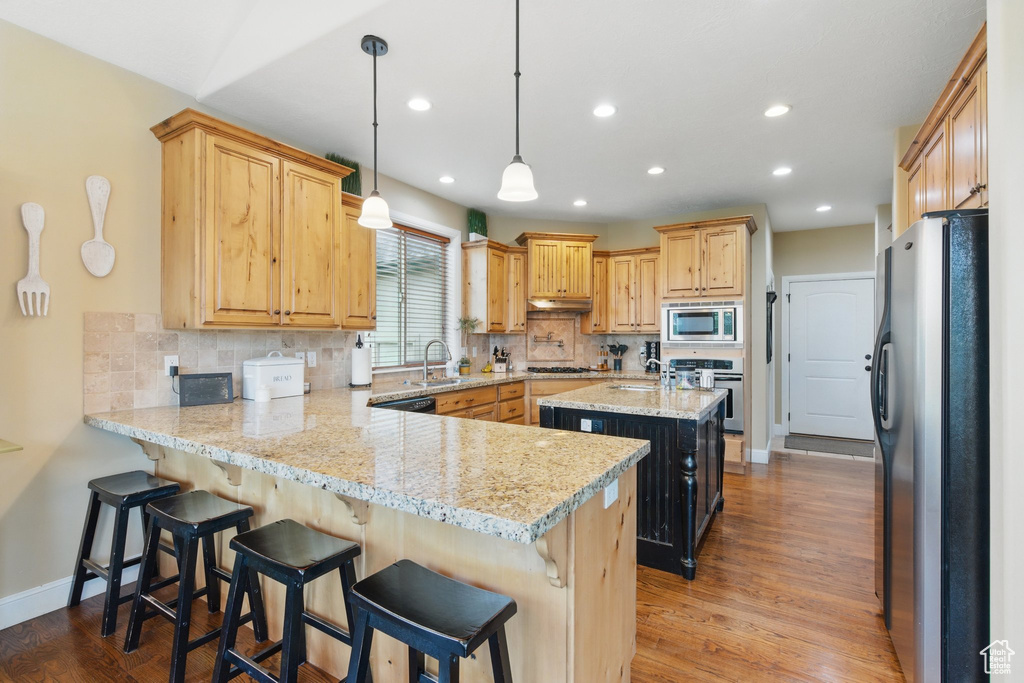 Kitchen with a peninsula, wood finished floors, recessed lighting, appliances with stainless steel finishes, and backsplash