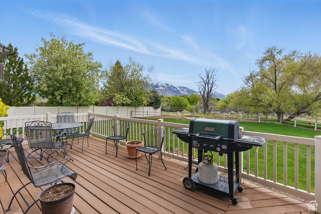 Wooden terrace featuring grilling area, a fenced backyard, a mountain view, outdoor dining area, and a yard