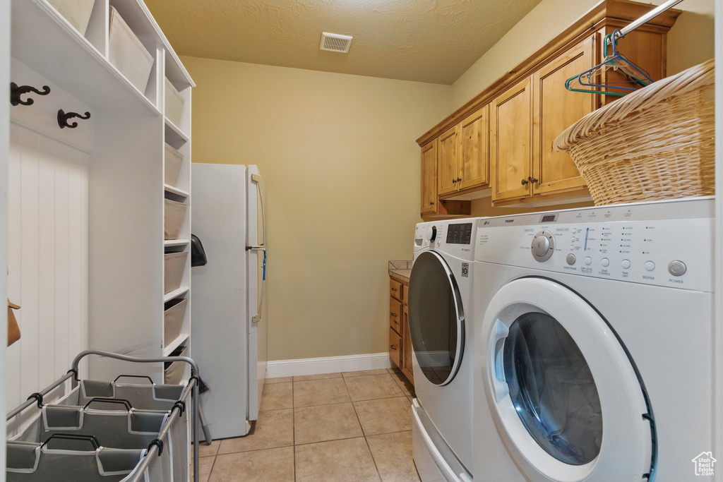 Laundry area featuring visible vents, baseboards, washing machine and clothes dryer, cabinet space, and light tile patterned floors
