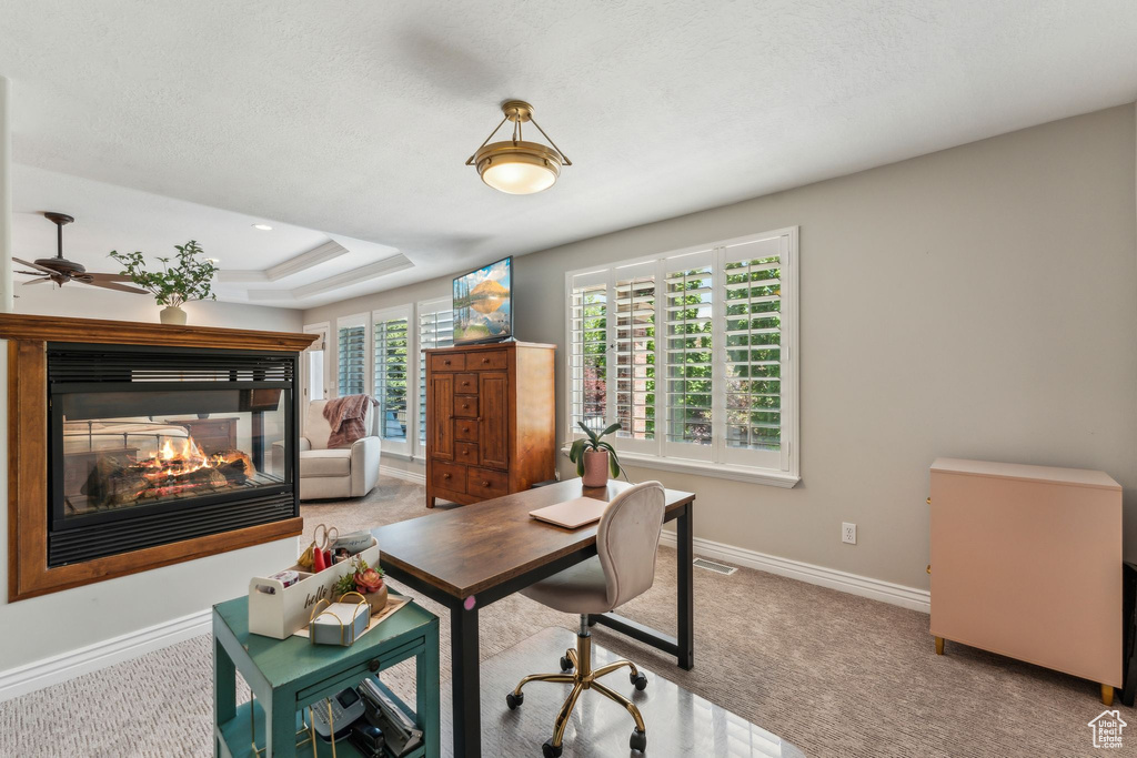 Carpeted office space featuring a multi sided fireplace, a ceiling fan, baseboards, and a tray ceiling