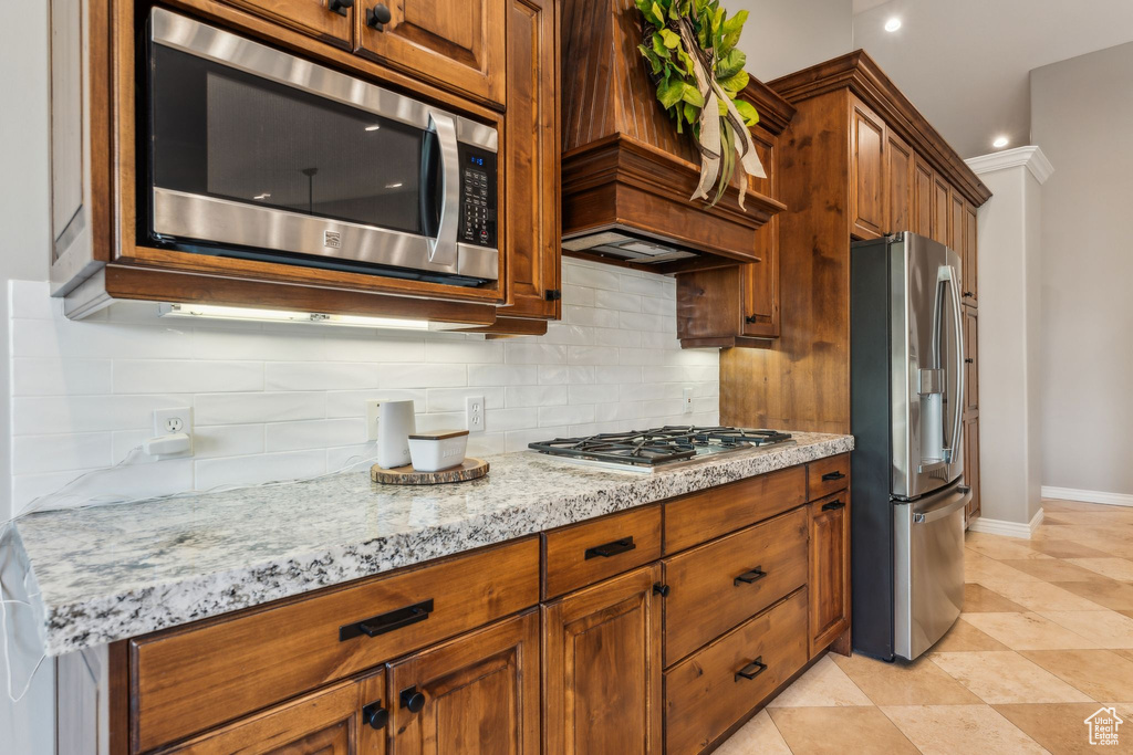 Kitchen with light stone countertops, stainless steel appliances, brown cabinets, and backsplash