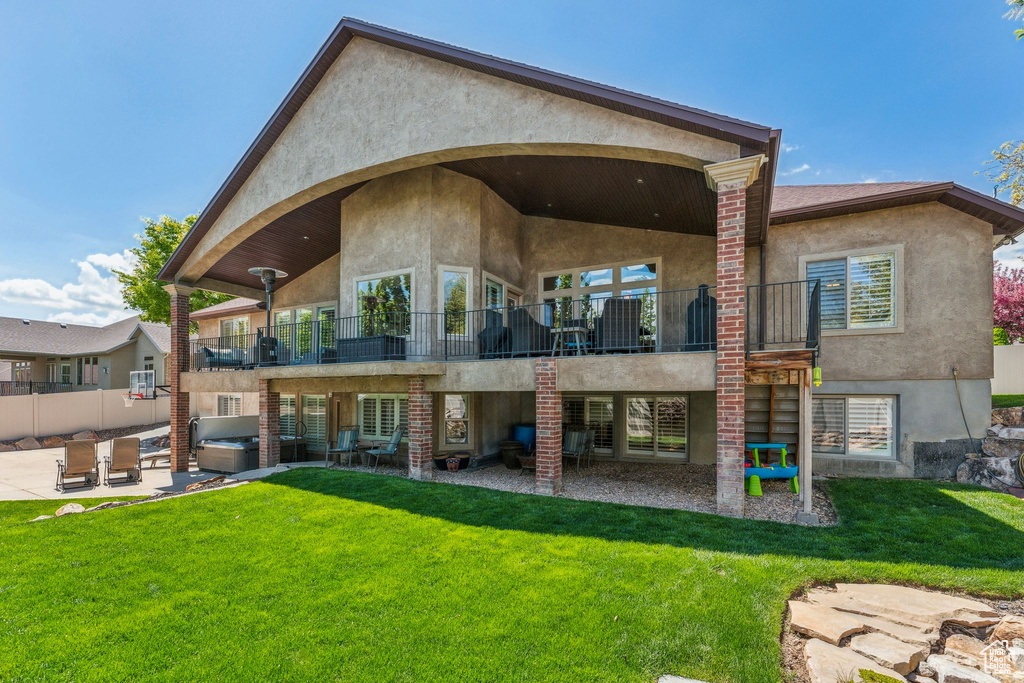 Rear view of house with a balcony, a patio, stucco siding, a lawn, and a hot tub