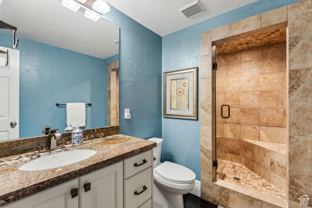Full bath with visible vents, vanity, a textured wall, toilet, and a shower stall