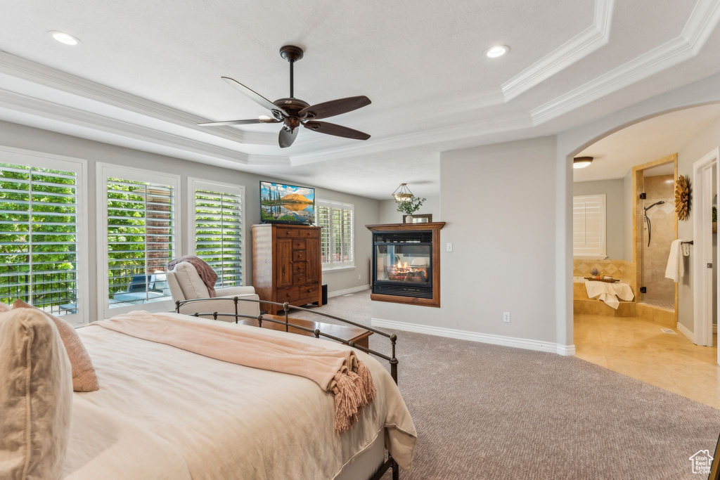 Carpeted bedroom with crown molding, a raised ceiling, arched walkways, a multi sided fireplace, and baseboards