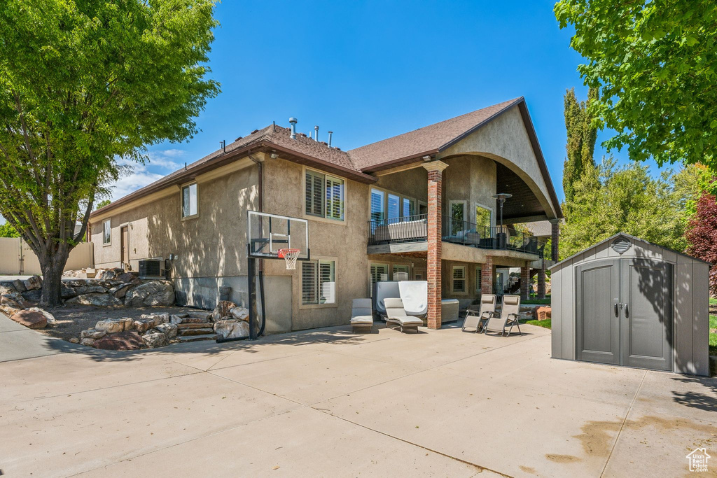 Back of house featuring a storage unit, stucco siding, a patio area, and a balcony