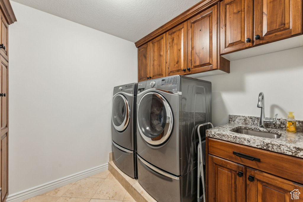 Clothes washing area with independent washer and dryer, cabinet space, a sink, light tile patterned floors, and baseboards
