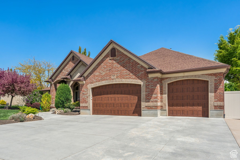 View of front facade with a garage, driveway, roof with shingles, and brick siding