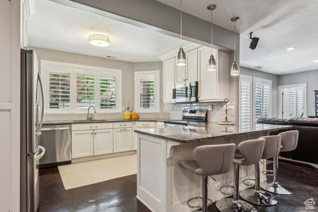 Kitchen featuring appliances with stainless steel finishes, a sink, dark stone counters, a peninsula, and backsplash