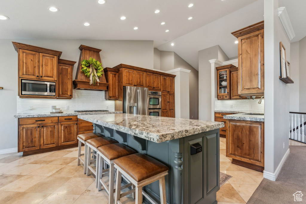Kitchen featuring brown cabinets, a center island, stainless steel appliances, tasteful backsplash, and vaulted ceiling
