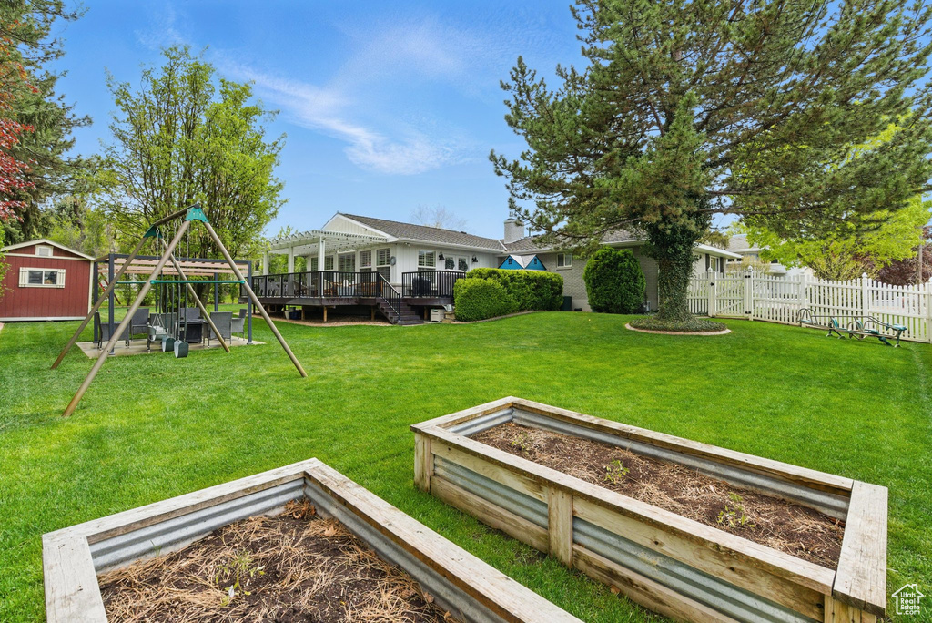View of yard with fence, a storage shed, a wooden deck, a garden, and a playground