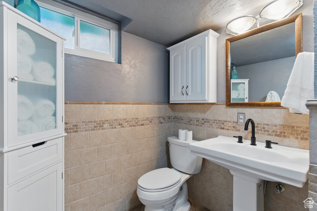 Bathroom featuring wainscoting, toilet, and tile walls