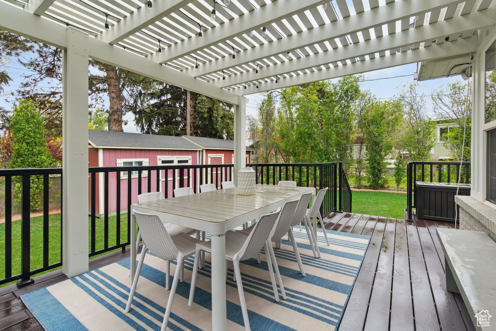 Wooden deck featuring a lawn, a pergola, an outbuilding, and outdoor dining area
