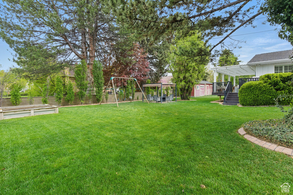 View of yard featuring an outdoor structure, fence, a pergola, a storage unit, and a playground