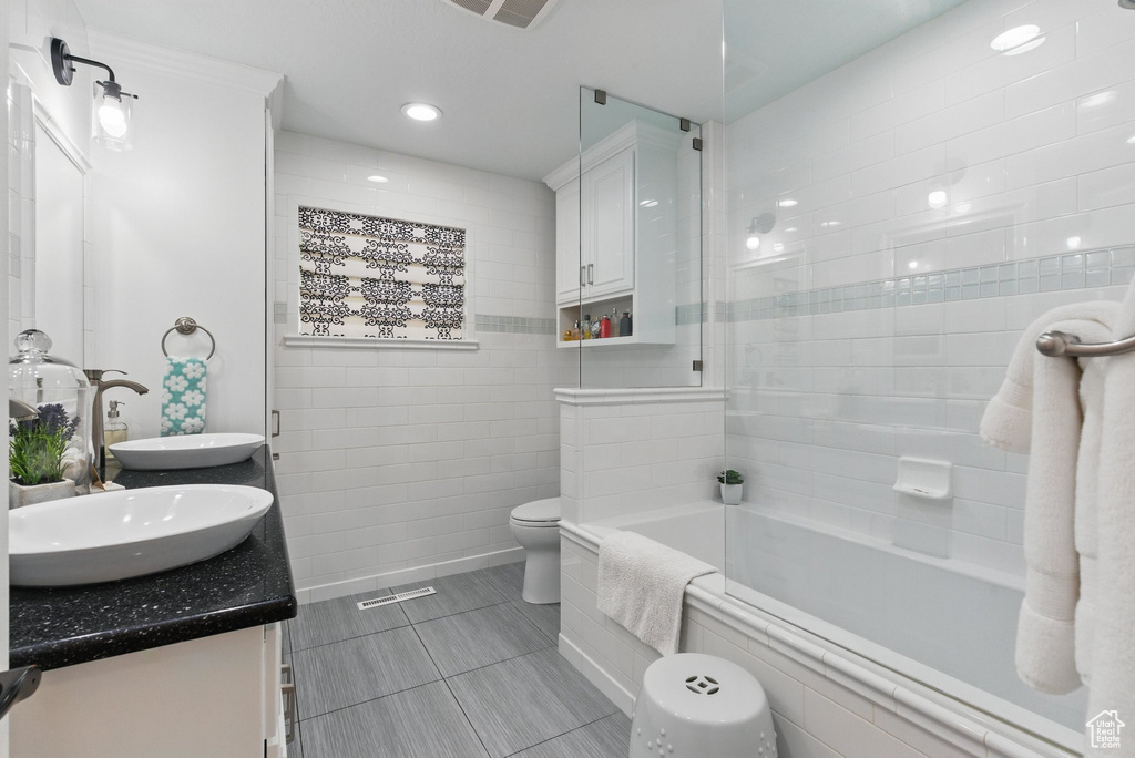 Full bathroom featuring double vanity, tile walls, a sink, tiled shower / bath, and toilet