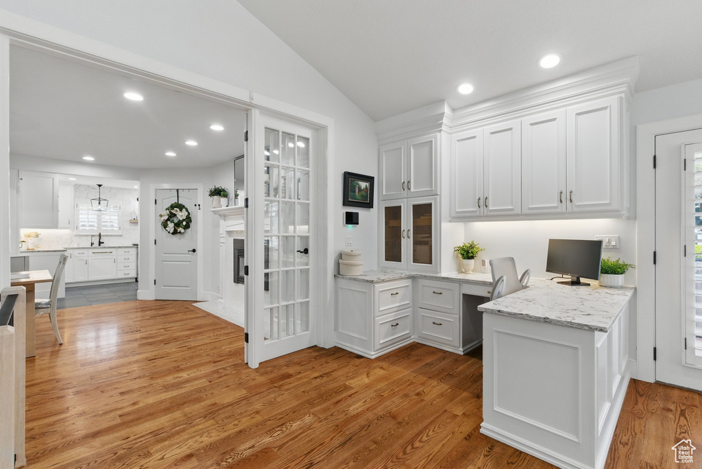 Kitchen with built in study area, light wood-type flooring, white cabinets, light stone counters, and vaulted ceiling