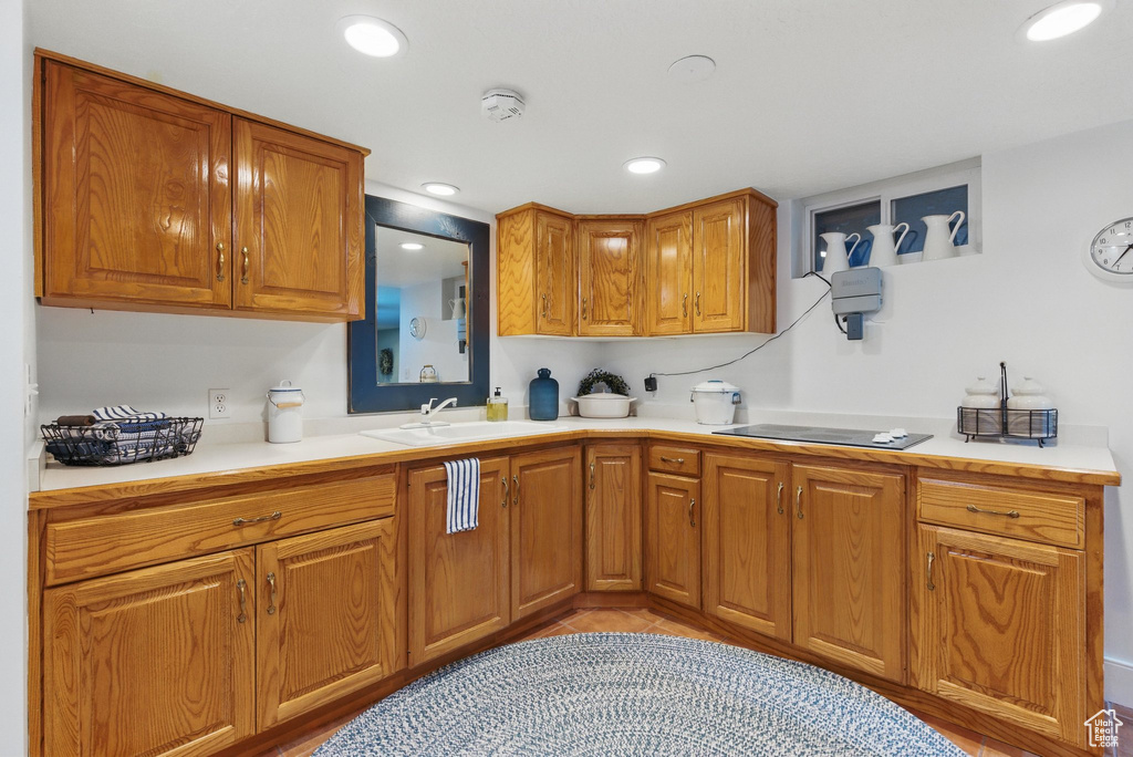 Kitchen with brown cabinetry, a sink, black electric cooktop, and light countertops