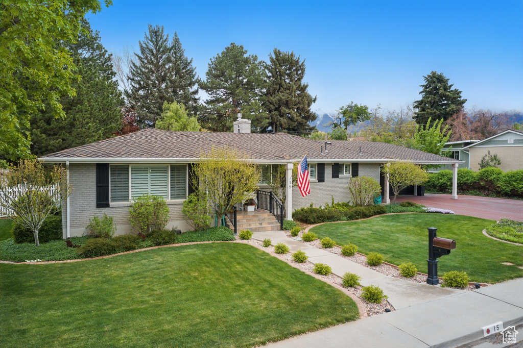 Ranch-style house with a front yard, an attached carport, a chimney, brick siding, and driveway
