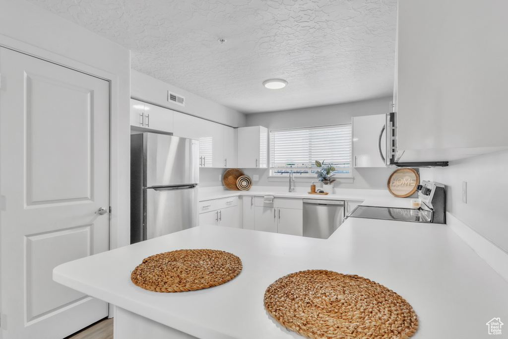 Kitchen with appliances with stainless steel finishes, light countertops, a textured ceiling, white cabinetry, and a peninsula
