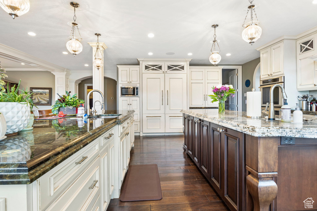 Kitchen featuring arched walkways, appliances with stainless steel finishes, a large island with sink, and a sink