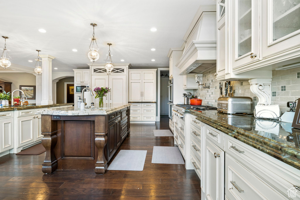 Kitchen featuring a sink, stainless steel gas cooktop, arched walkways, a kitchen island with sink, and recessed lighting