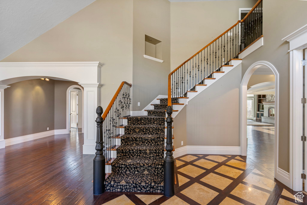 Stairway with baseboards, arched walkways, a high ceiling, and hardwood / wood-style flooring