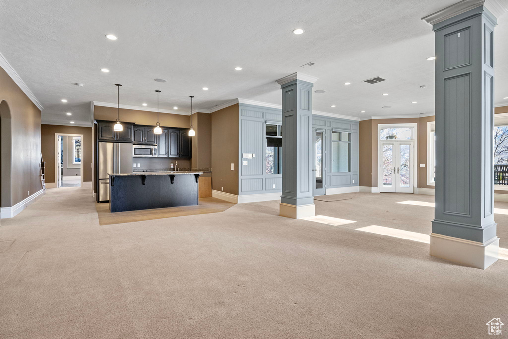 Unfurnished living room with crown molding, light carpet, recessed lighting, baseboards, and decorative columns
