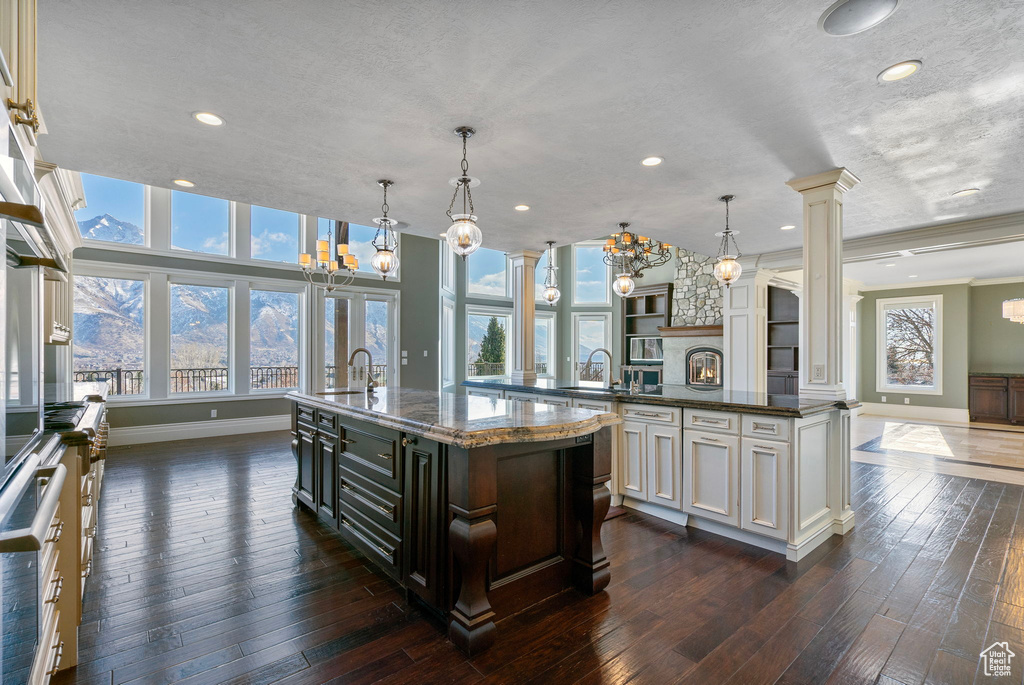 Kitchen with decorative columns, baseboards, recessed lighting, a large island with sink, and dark wood finished floors