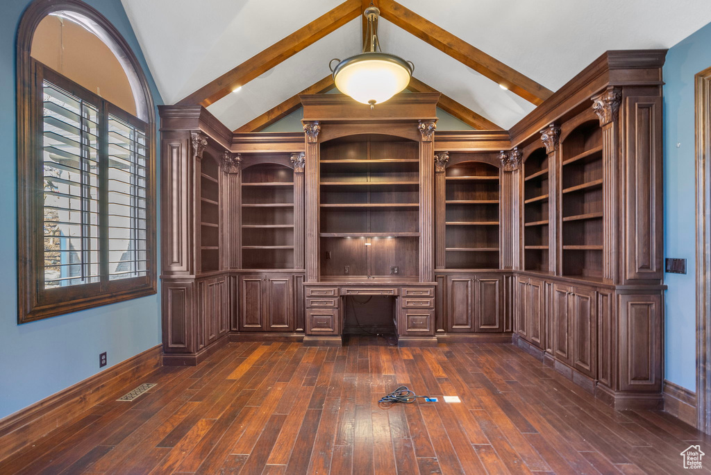 Interior space with built in desk, baseboards, lofted ceiling, visible vents, and dark wood-style floors