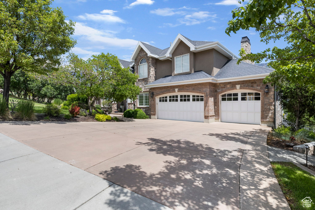 View of front facade featuring stone siding, stucco siding, a chimney, a shingled roof, and driveway
