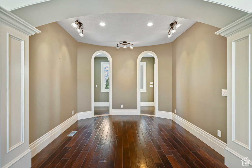 Unfurnished room featuring arched walkways, rail lighting, baseboards, dark wood-type flooring, and visible vents