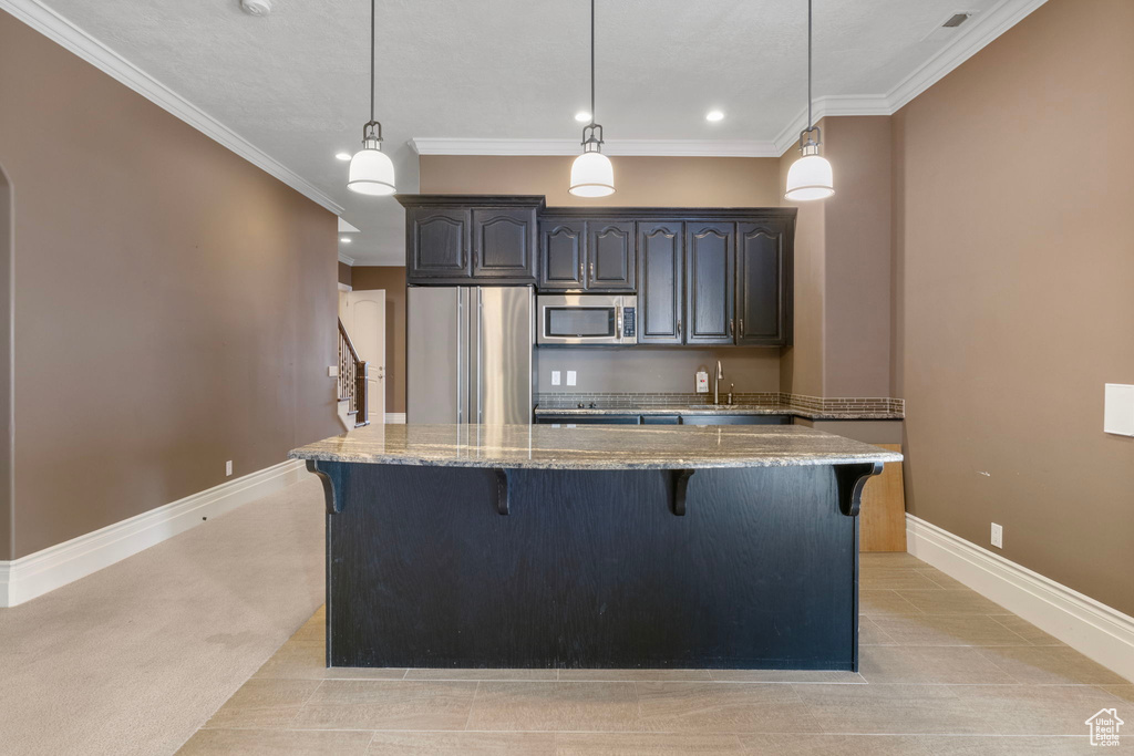 Kitchen with a breakfast bar, baseboards, a center island, light stone counters, and appliances with stainless steel finishes