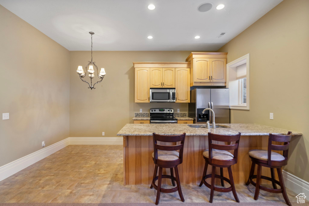 Kitchen featuring light brown cabinetry, a breakfast bar, baseboards, a sink, and stainless steel appliances