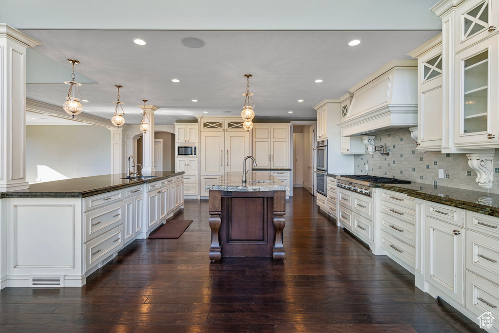 Kitchen featuring a breakfast bar area, custom range hood, a large island with sink, a sink, and appliances with stainless steel finishes