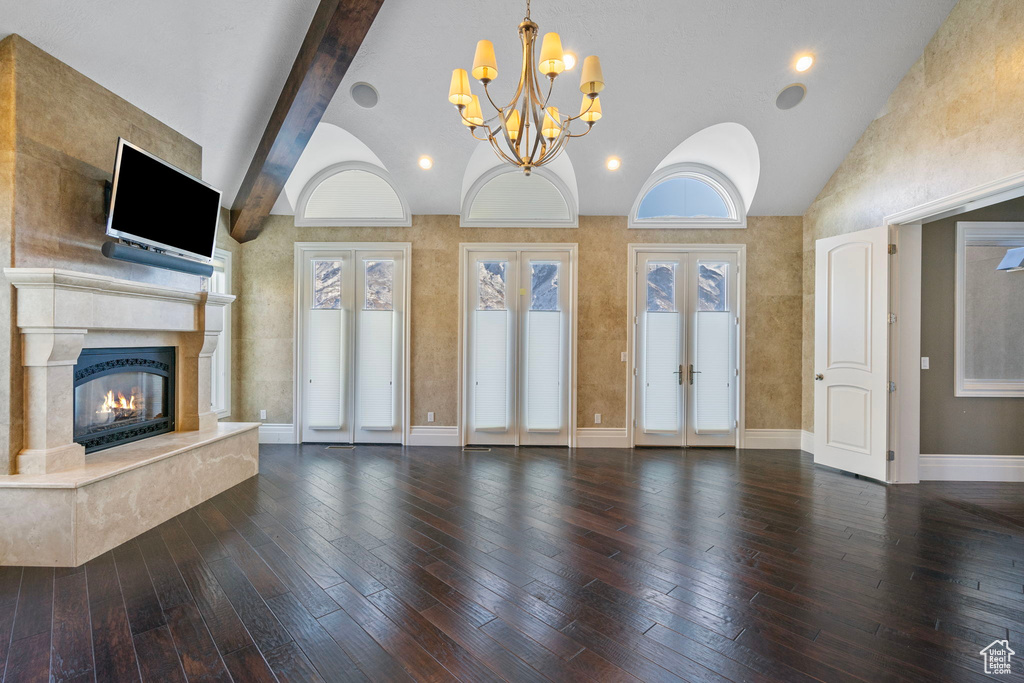 Unfurnished living room featuring an inviting chandelier, hardwood / wood-style flooring, french doors, lofted ceiling with beams, and a premium fireplace