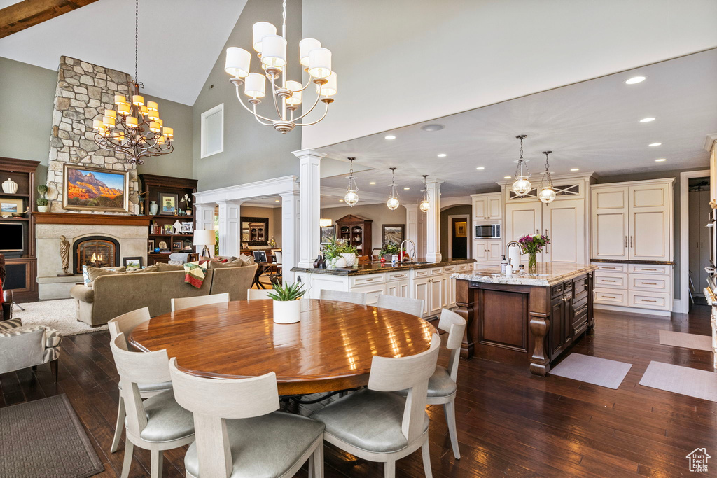 Dining space featuring dark wood-type flooring, a fireplace, a chandelier, and high vaulted ceiling