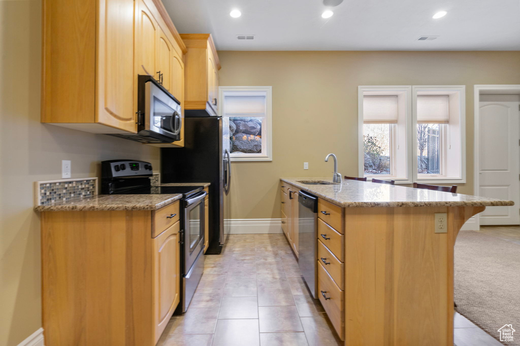 Kitchen featuring light brown cabinetry, baseboards, light stone counters, a sink, and appliances with stainless steel finishes