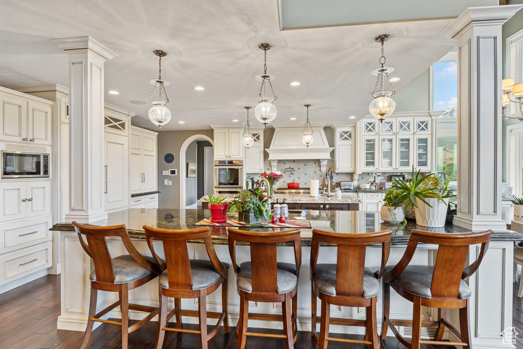 Kitchen with appliances with stainless steel finishes, tasteful backsplash, a large island with sink, custom range hood, and recessed lighting