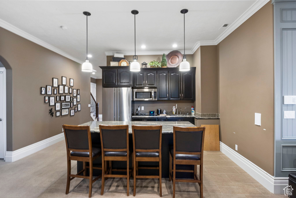 Kitchen featuring arched walkways, appliances with stainless steel finishes, a breakfast bar, and ornamental molding