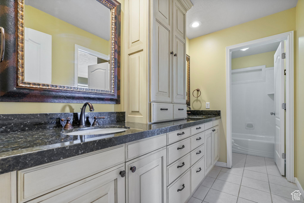 Full bath with double vanity, tile patterned flooring, a sink, baseboards, and a tub to relax in