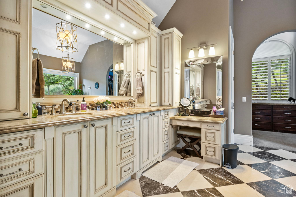 Full bath with double vanity, a sink, a chandelier, and vaulted ceiling