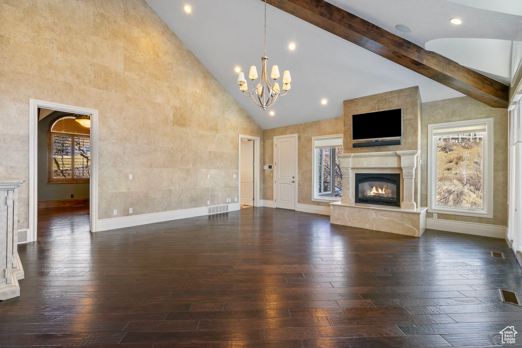 Unfurnished living room with high vaulted ceiling, a chandelier, dark wood finished floors, baseboards, and a high end fireplace