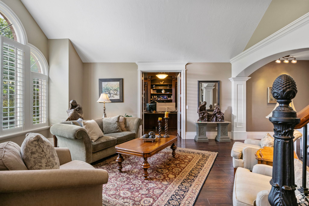 Living room with dark wood-style flooring, arched walkways, vaulted ceiling, and decorative columns