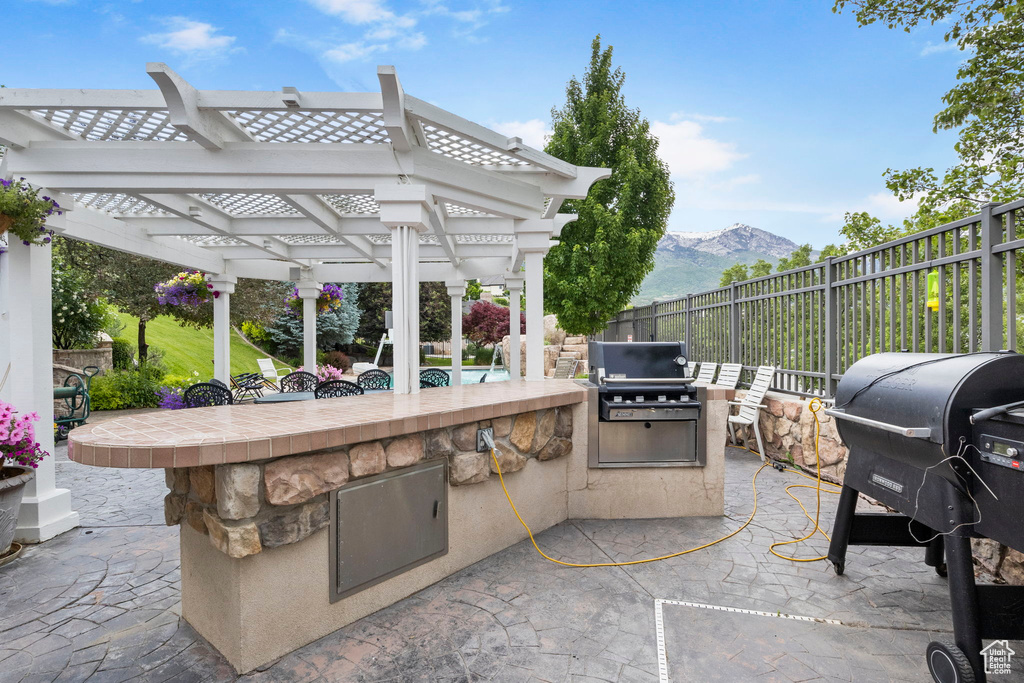 View of patio featuring fence, a pergola, area for grilling, exterior kitchen, and a mountain view