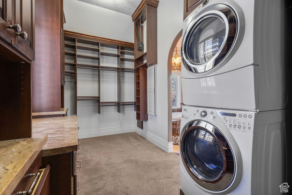 Washroom featuring light colored carpet, baseboards, cabinet space, and stacked washer / drying machine