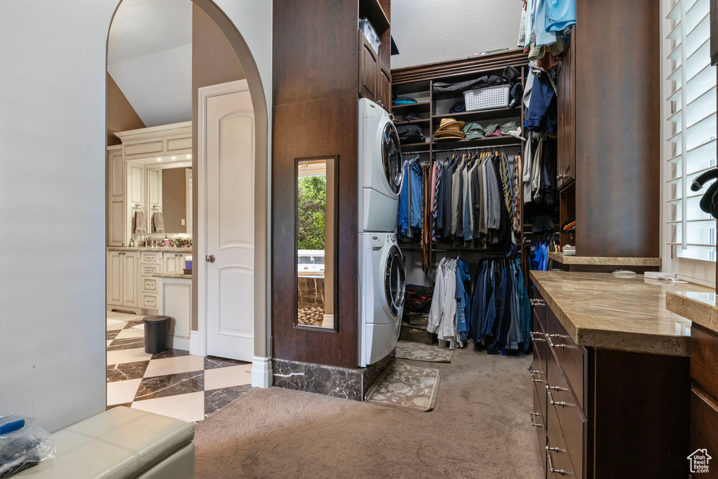 Walk in closet featuring arched walkways, stacked washer / dryer, and lofted ceiling