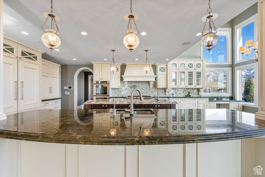 Kitchen featuring arched walkways, backsplash, custom exhaust hood, and recessed lighting